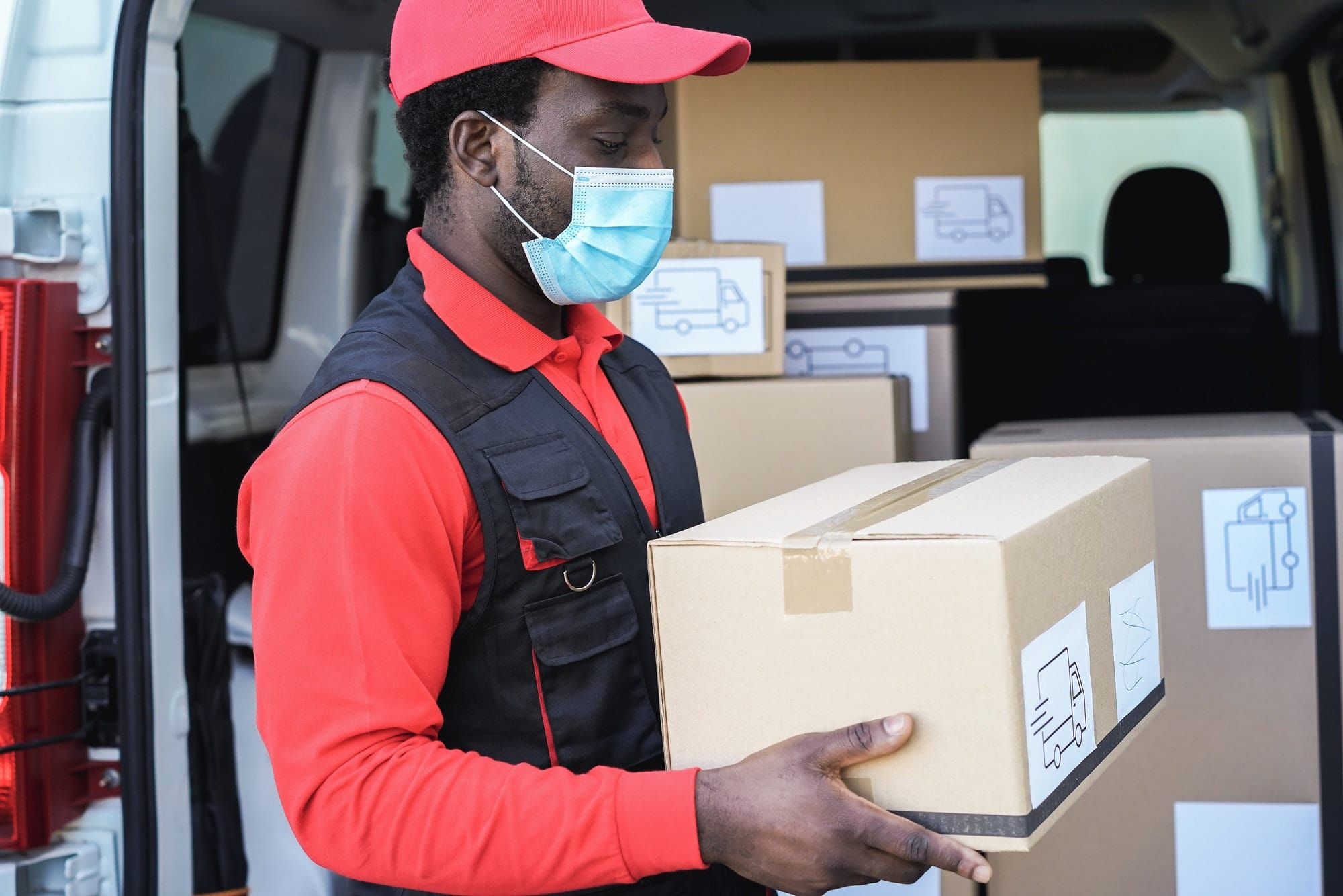 Black delivery man wearing safety mask for coronavirus prevention - Focus on face